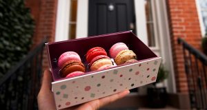 A box full of macarons has a macaron box with a thank you sleeve to the left.