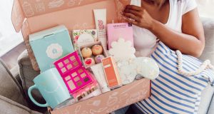 A smiling woman is holding a box full of assorted accessories. https://www.allsubscriptionboxes.co.uk/fabfitfun/ 
