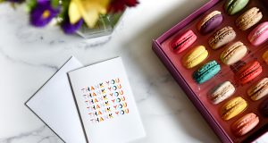 A box full of French macarons has a Thank You greeting card to the left. At the top are some flowers.