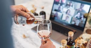 A man is pouring a cup of wine in front of a computer. https://ingoodtaste.com/pages/wine-tasting-events 