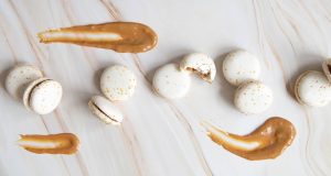 Several white Dulce de Leche macarons are surrounded by splashes of dulce de leche. 