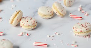Several white Peppermint French macarons are surrounded by candy canes. 