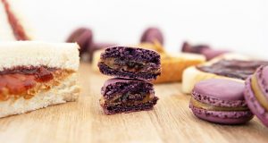 Several purple Peanut Butter & Jelly French macarons are surrounded by PB&J sandwiches.