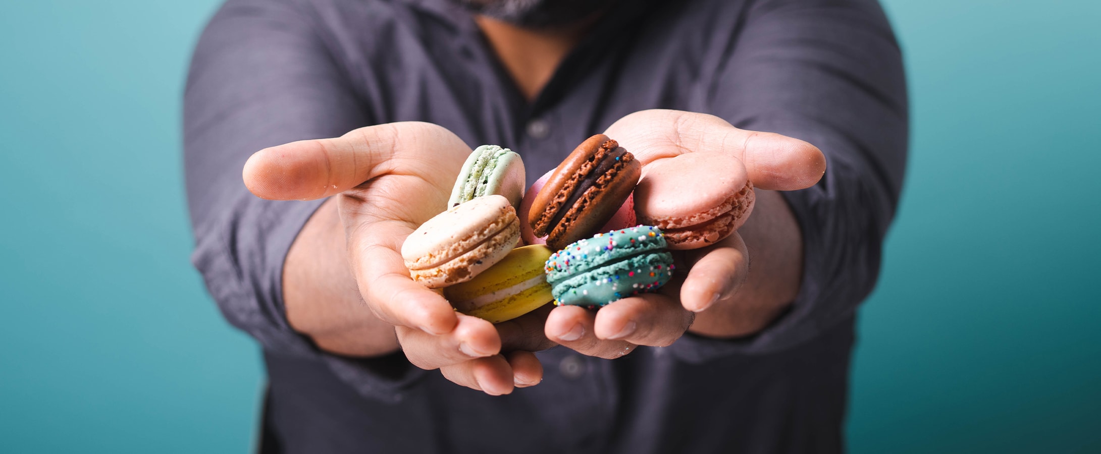 A smiling man is holding some assorted French macarons in his hands.