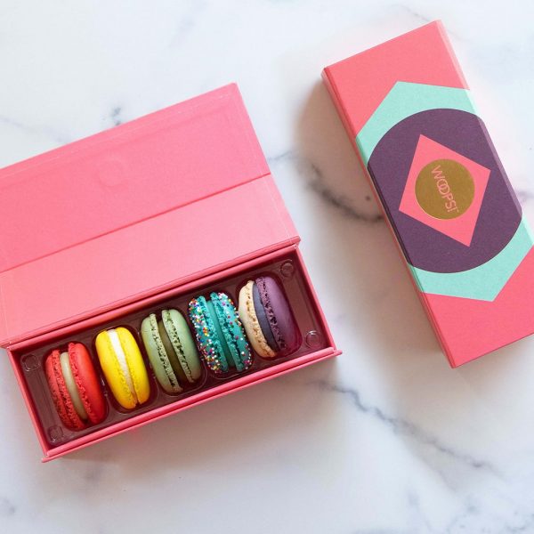 A box full of five assorted macarons has a pink macaron box to the right.