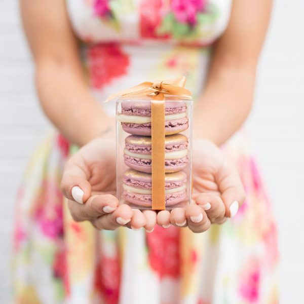 A woman in a flowered dress is holding a favor box with three French macarons on her hands.