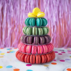 A French macaron pyramid with assorted flavors has a pink background.