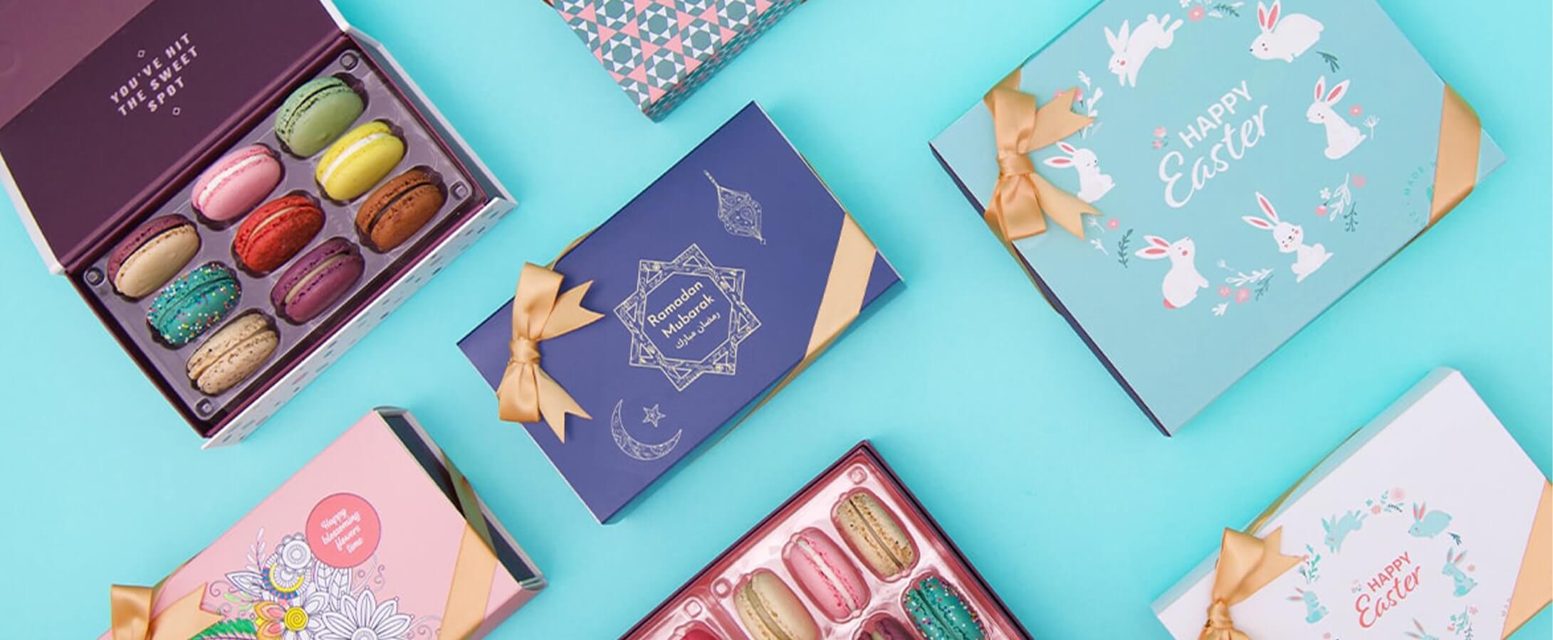 Two Woops! boxes full of assorted macarons are surrounded by macaron boxes with Easter, Blossoming Colors, Passover, and Ramadan & Eid sleeves.