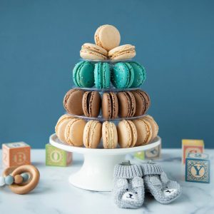 A small pyramid with Vanilla, Mint Chocolate, and Dark Chocolate French macarons is surrounded by baby toys.