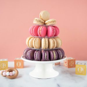 A small pyramid with Vanilla, Rose, and Strawberry French macarons is surrounded by baby toys.