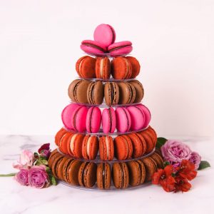 A large French macaron pyramid with Milk Chocolate, Dark Chocolate, Red Velvet, and Nutella macarons has some flowers on its base.