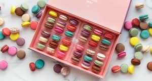 A box full of 36 French macarons is surrounded by numerous assorted French macarons.