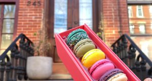 A box full of assorted Woops! macarons is being held in front of a doorstep.