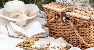 A picnic basket has a cheeseboard, a book, and a hat in front.