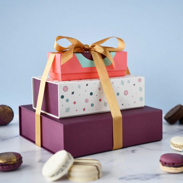 A box of 3 and 18 French macaron box with an Argentinian alfajores box stacked up with a golden ribbon holding them together, and some assorted French macarons and alfajores lying around.