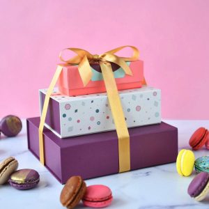 A stack of three French macaron boxes is surrounded by assorted French macarons.