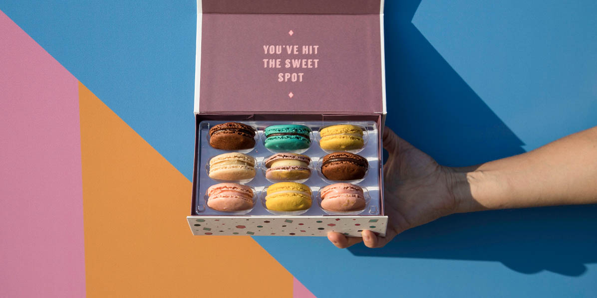 A hand is holding a Woops! French macaron box