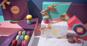 A box full of assorted French macarons is surrounded by numerous French macaron boxes and assorted macarons. 