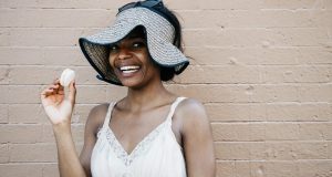  A smiling woman with a hat and glasses is holding a French macaron in her hand