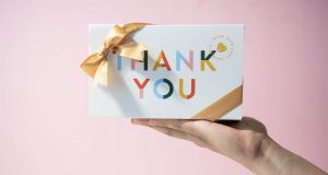 A hand is holding a Woops! French macaron box with a Thank You sleeve. 