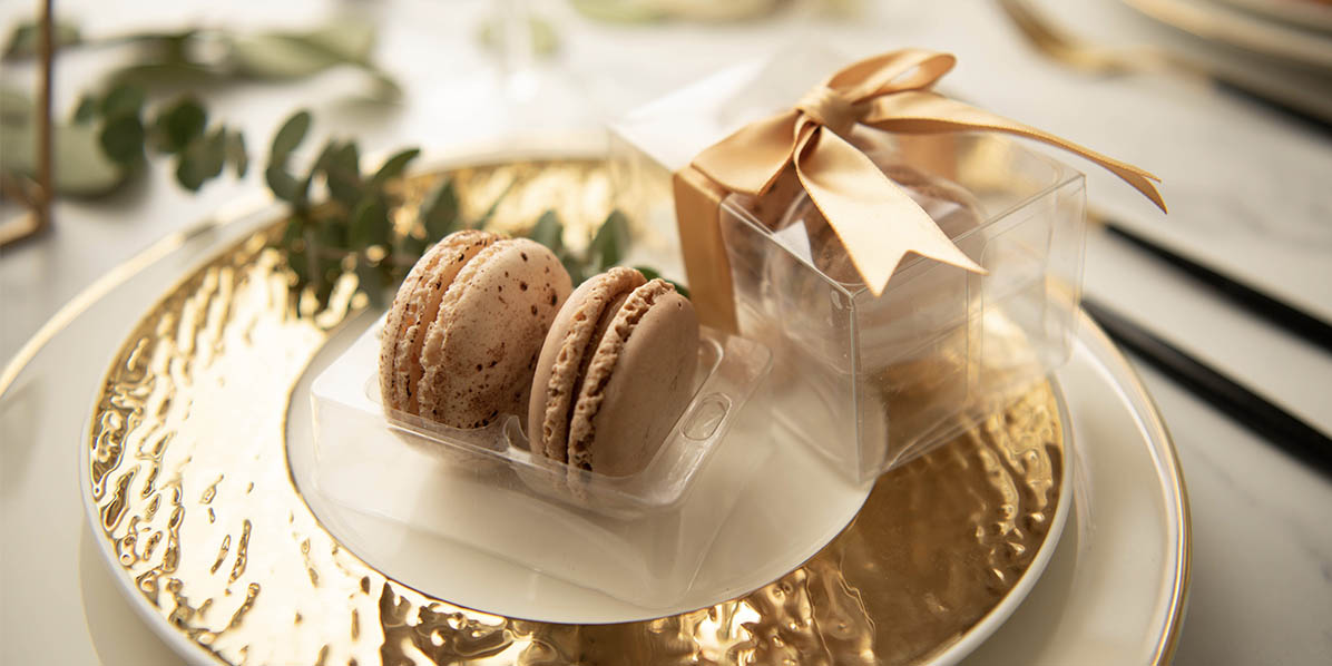 A golden plate has a box of two French macarons on top.