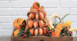 A French macaron pyramid on a wooden cart is surrounded by pumpkins and plants.
