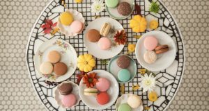 Several plates full of assorted macarons are surrounded by flowers.
