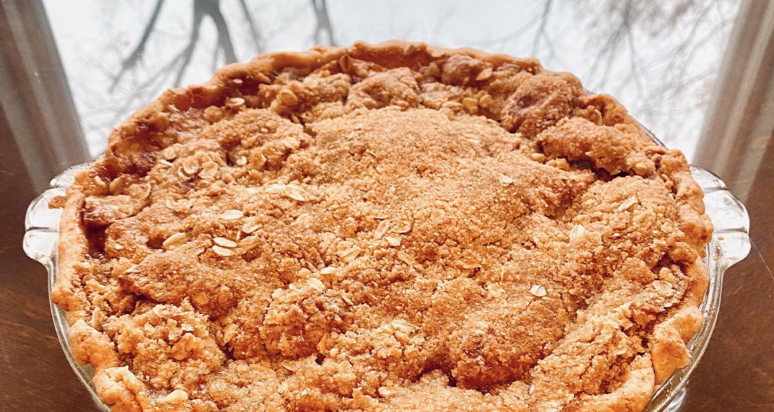 Homemade apple pie on a glass table with trees and sky background in reflection. 