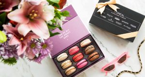 A box full of macarons has a macaron box with a custom L’Oreal sleeve to the side. A clock and some flowers are on the sides.