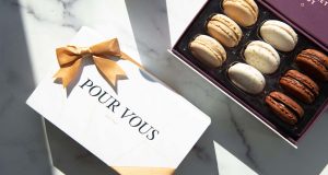  A box full of macarons has a macaron box with a Pour Vous sleeve and a golden ribbon to the side. 