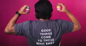A man with a Woops! “good things come to those who bake” t-shirt is holding French macarons in his hands.