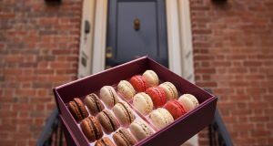 A big box full of French macarons in front of a doorstep. 