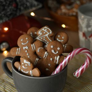 A cup is full of gingerbread cookies and a peppermint bark. Surrounding it are numerous Christmas decorations