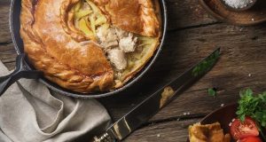 Meat pie with a knife, napkin, and vegetables to its sides