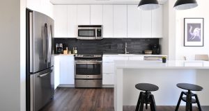 Black and white kitchen with bar, stools, fridge, lamps, and kitchen equipment