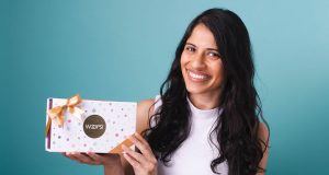 A smiling woman with long black hair is holding a Woops! Macaron box in her hands.