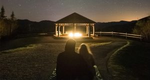 A couple is stargazing, in front of them is a small kiosk with a fire