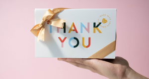 A hand is holding a box of macarons with a Thank You sleeve