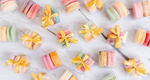 Numerous favor boxes of two French macarons with yellow ribbons.