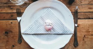 A plate with a napkin and a pink Easter egg has cutlery on its sides.
