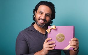 A smiling man is holding a purple Woops! Macaron gift box