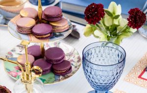 A tiered tray with Honey Lavender French macarons is surrounded by glasses, flowers, and table decorations.
