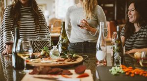 Smiling women around a dinner table filled with bottles of wine and food.