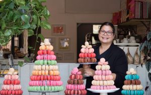 A smiling woman with several French macaron pyramids in front of her.