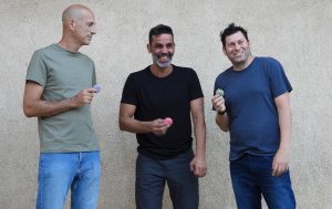 Three smiling men holding French macarons in their hands. 