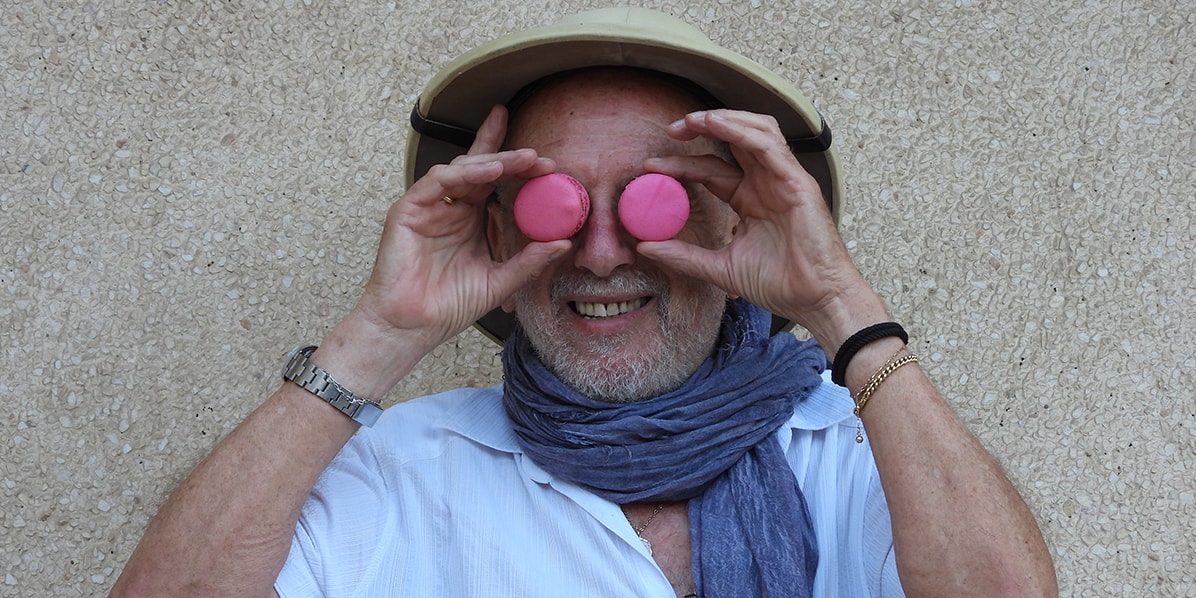 A smiling man is holding two French macarons to his eyes