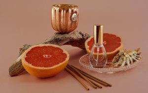 Two red tangerine surrounded by a candle, seashells, and oil essentials.