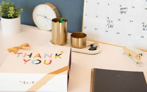 A macaron box with a Thank You sleeve is surrounded by office essentials. 