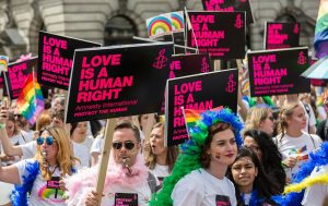 Numerous people holding black and pink signs while dressed in Pride colors.