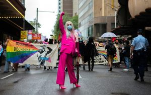 A woman dressed in pink with a Pride parade behind her.